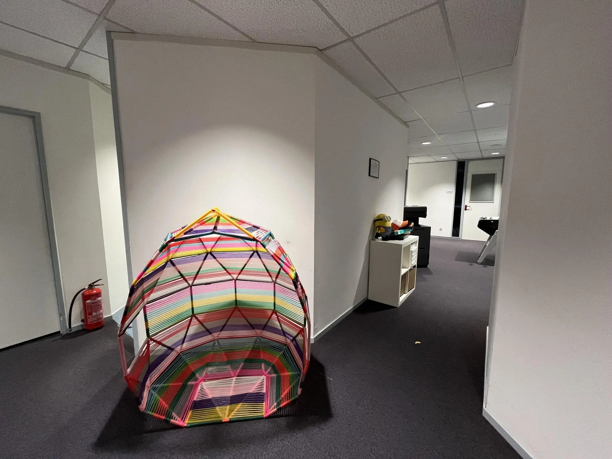 Gekleurde koepelvormige constructie van stokken en touw in een kantoorruimte aan de Industrieweg.