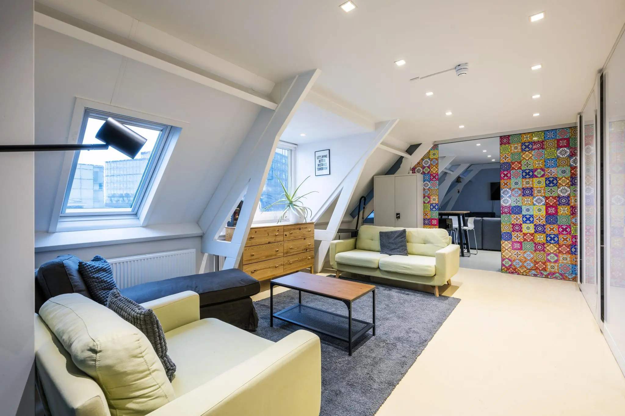 Modern ingerichte woonkamer op De Ruijterkade met schuine plafonds, lichte meubels en een kleurrijke betegelde muur.