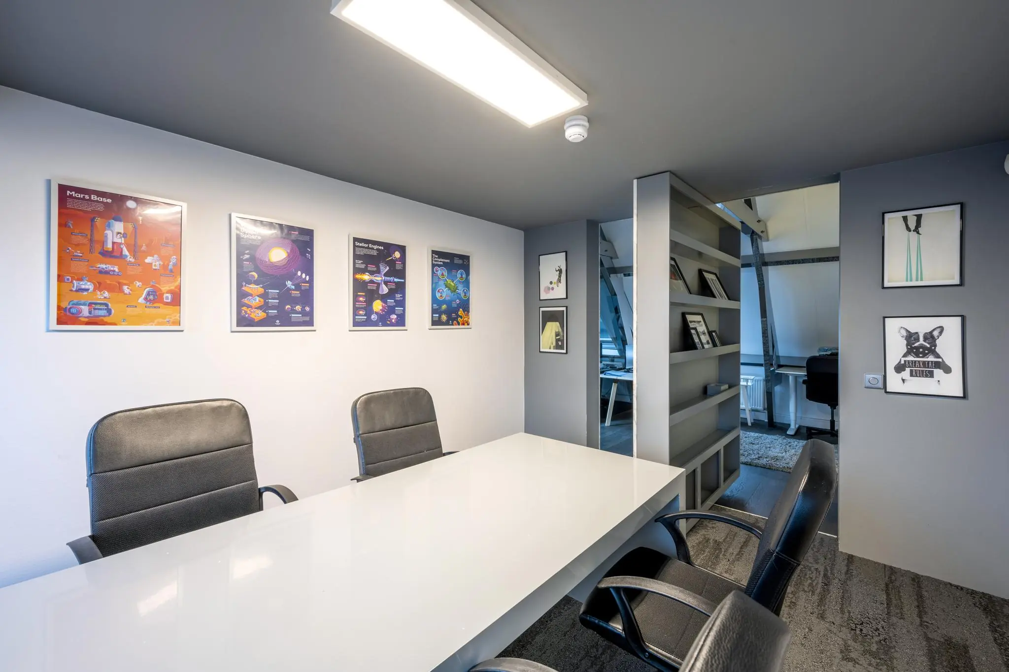 Vergaderruimte aan de De Ruijterkade met moderne inrichting, designstoelen, witte tafel en kleurrijke posters aan de muur.