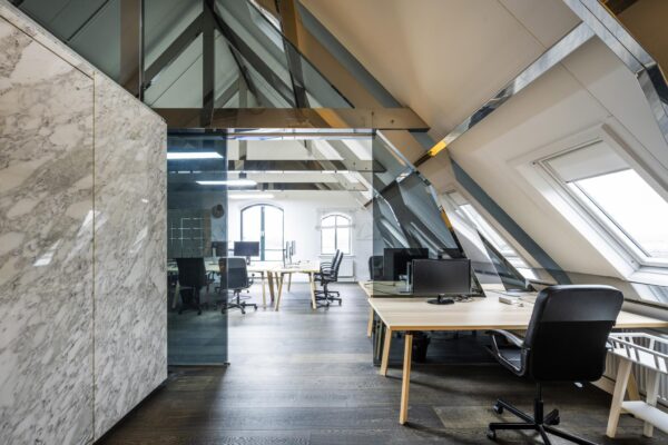 Modern kantoorinterieur aan de De Ruijterkade met schuine plafonds, glazen wanden en werkplekken met computers.