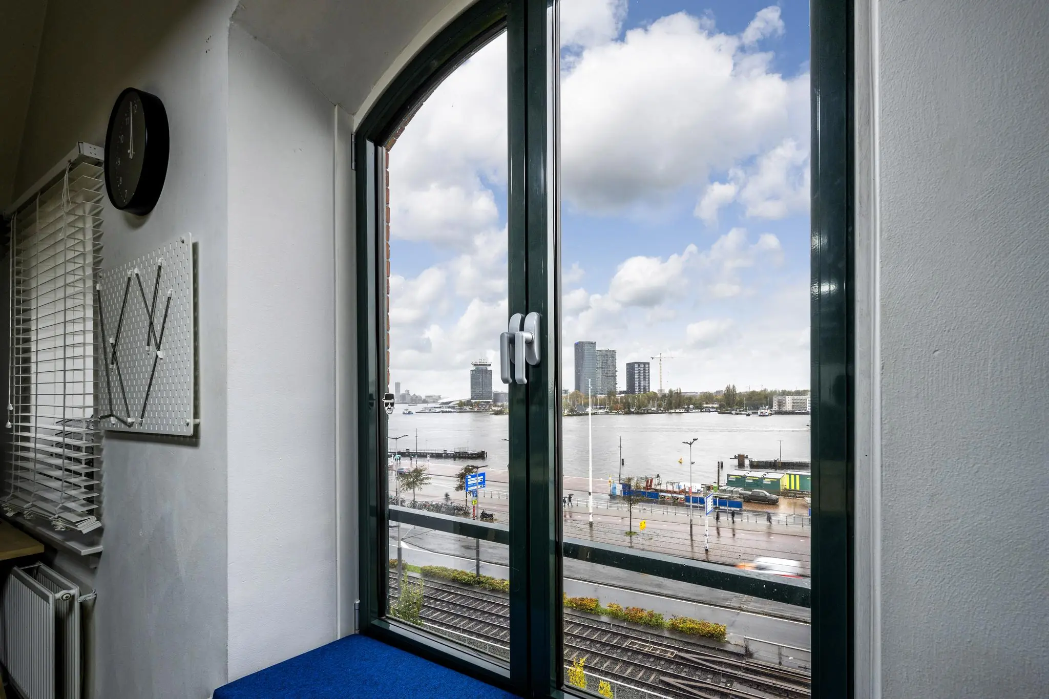 Uitzicht vanuit een raam aan de De Ruijterkade op het IJ en moderne gebouwen aan de overkant van het water.