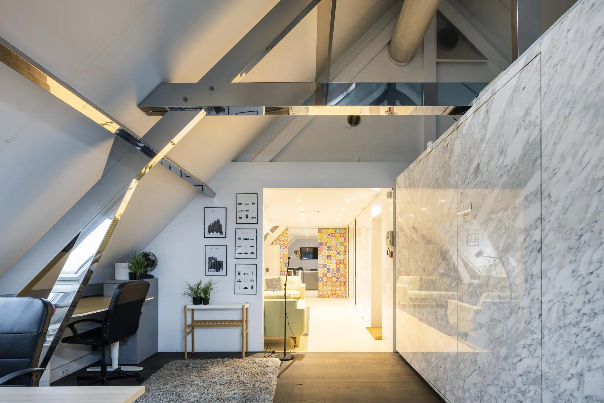 Modern ingerichte zolderruimte aan de De Ruijterkade met werkplek, marmeren wand en kleurrijke tegelmuur op de achtergrond.