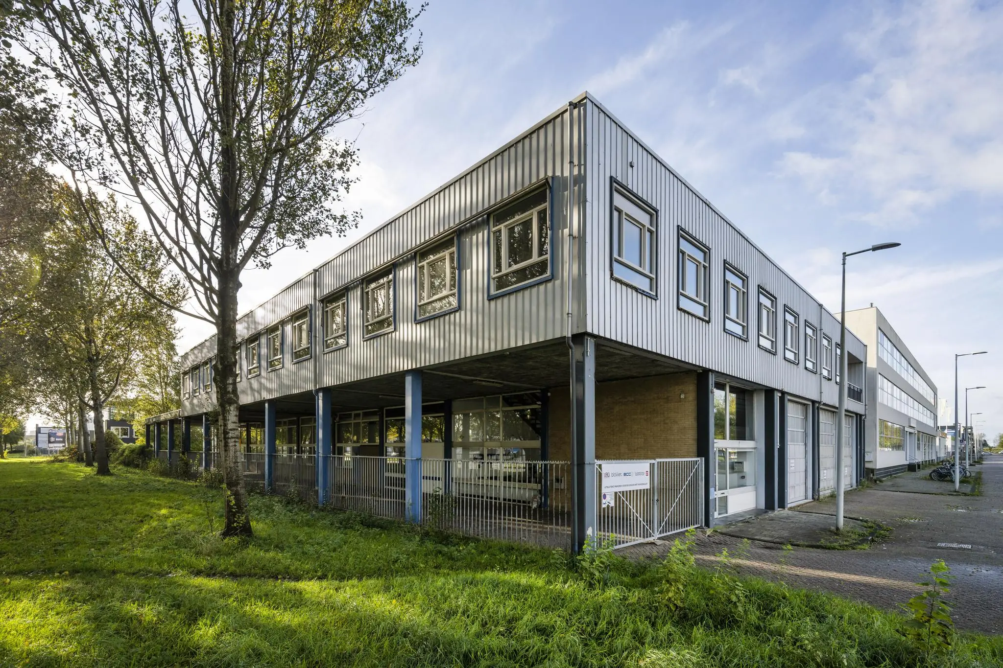 Zakelijk bedrijfsgebouw aan de Van der Madeweg met metalen gevel en blauwe steunpilaren.