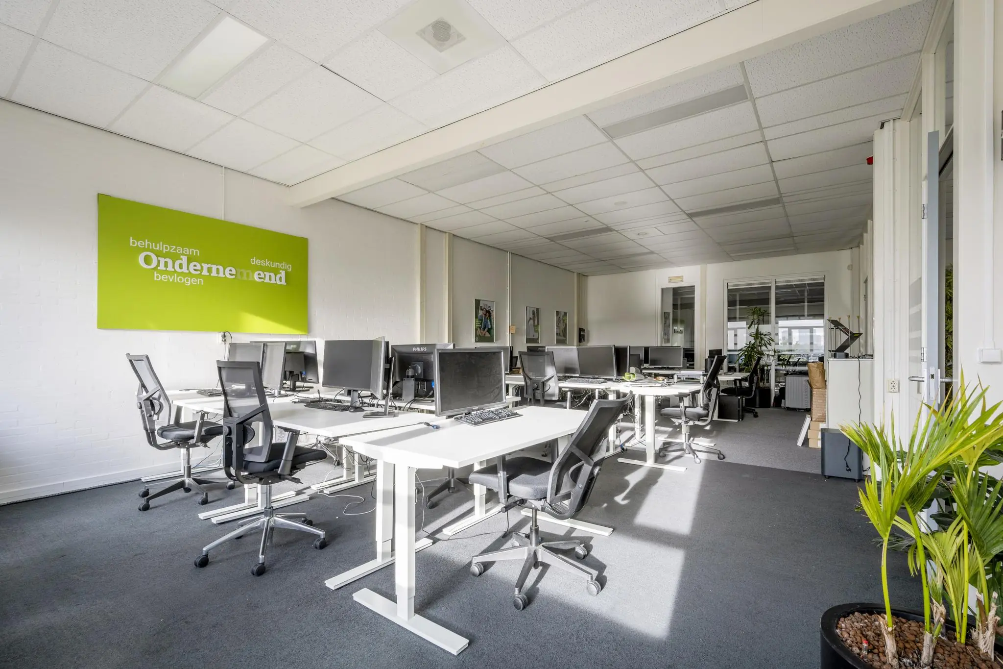 Licht en modern kantoor aan de Van der Madeweg met meerdere werkplekken, computers en een groene inspiratiewand.
