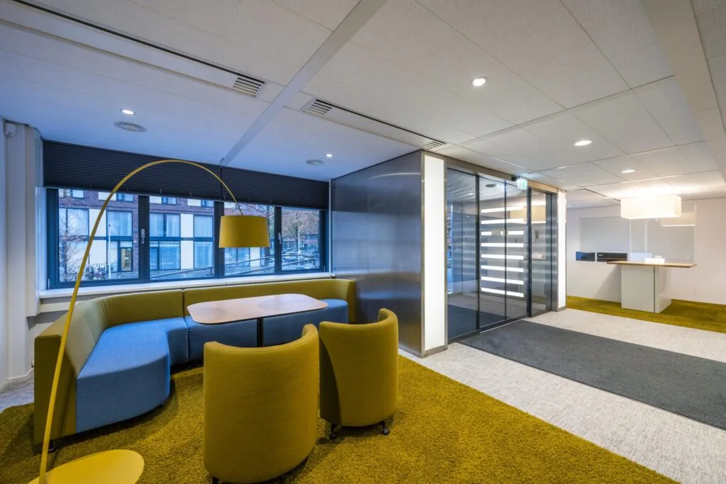 Moderne kantoorlobby met kleurrijk meubilair, glazen schuifdeuren en grote ramen aan de Stroombaan.