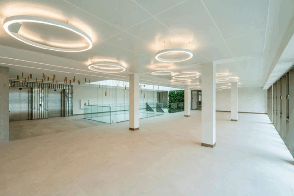 Lichte en moderne entreehal van het Walborg-gebouw met ringvormige plafondverlichting en glazen trapafscheiding.