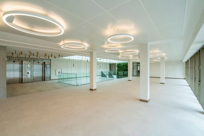 Lichte en moderne entreehal van het Walborg-gebouw met ringvormige plafondverlichting en glazen trapafscheiding.