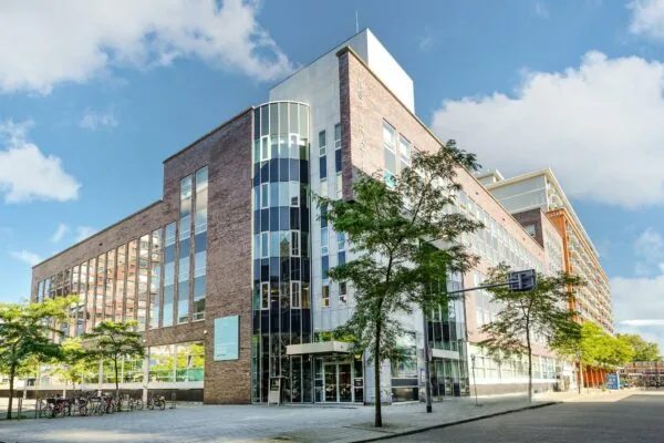 Modern kantoorgebouw aan de Dynamostraat met grote glaspartijen en bomen langs de stoep.