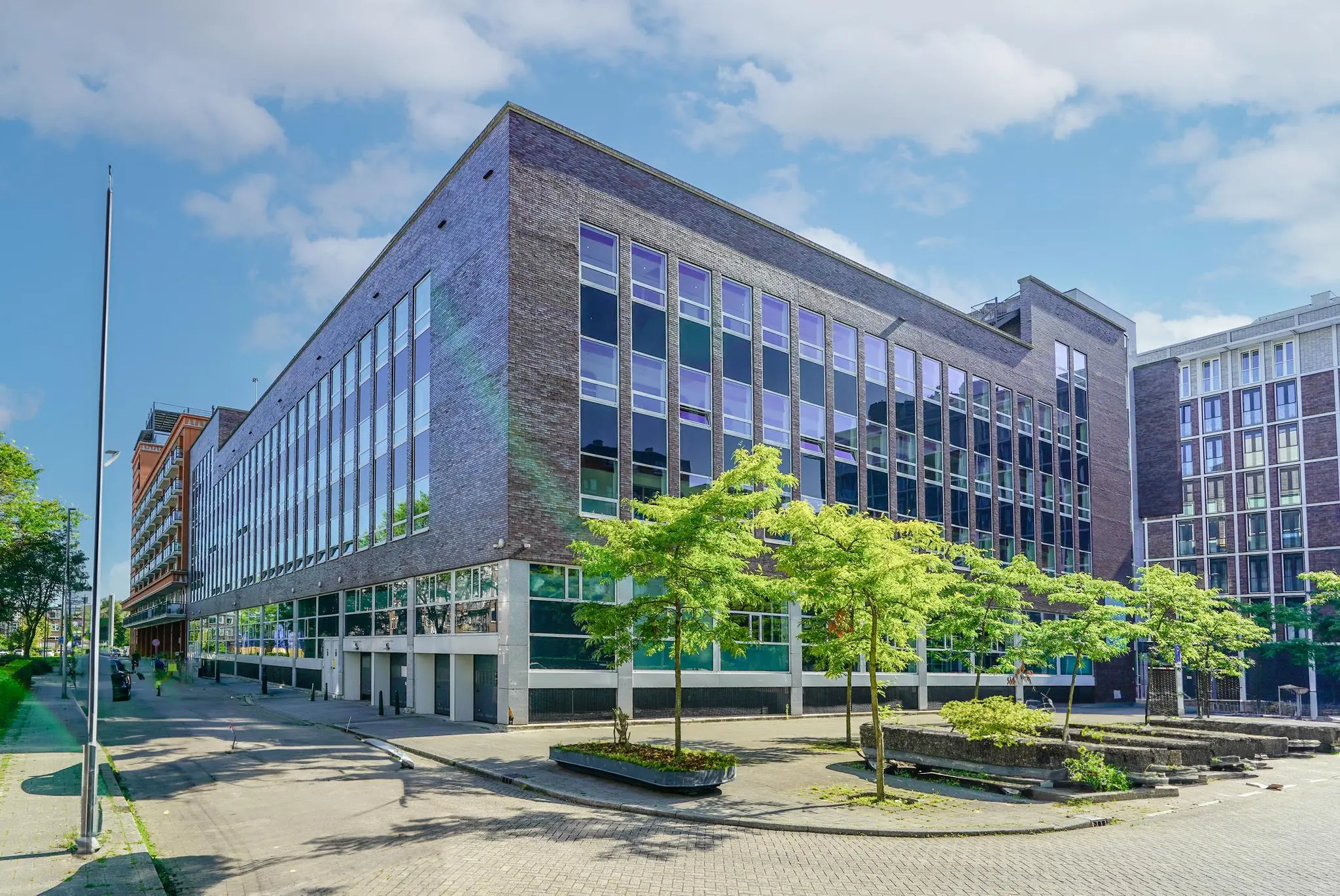 Modern kantoorgebouw aan de Dynamostraat met grote glaspartijen en omliggende jonge bomen.