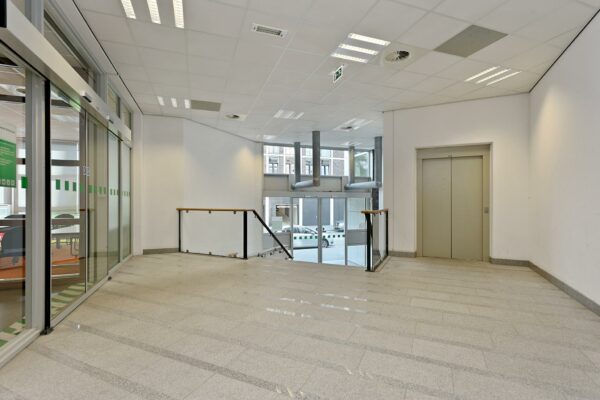 Ingangsruimte met lift, trap en glazen schuifdeur in een kantoorgebouw aan de Dynamostraat.