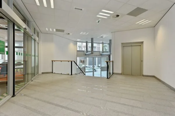 Ingangsruimte met lift, trap en glazen schuifdeur in een kantoorgebouw aan de Dynamostraat.