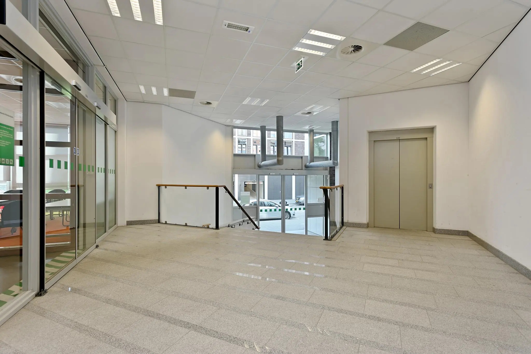 Ingangsruimte met lift, trap en glazen schuifdeur in een kantoorgebouw aan de Dynamostraat.