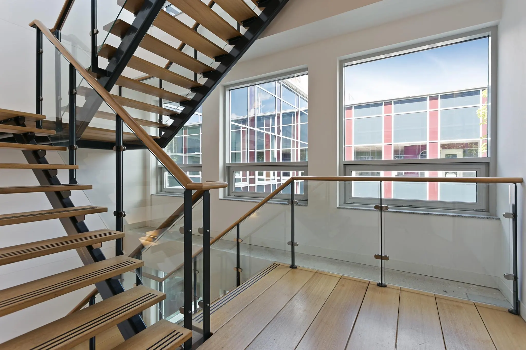 Moderne houten trap met glazen balustrade in een licht trappenhuis aan de Dynamostraat.