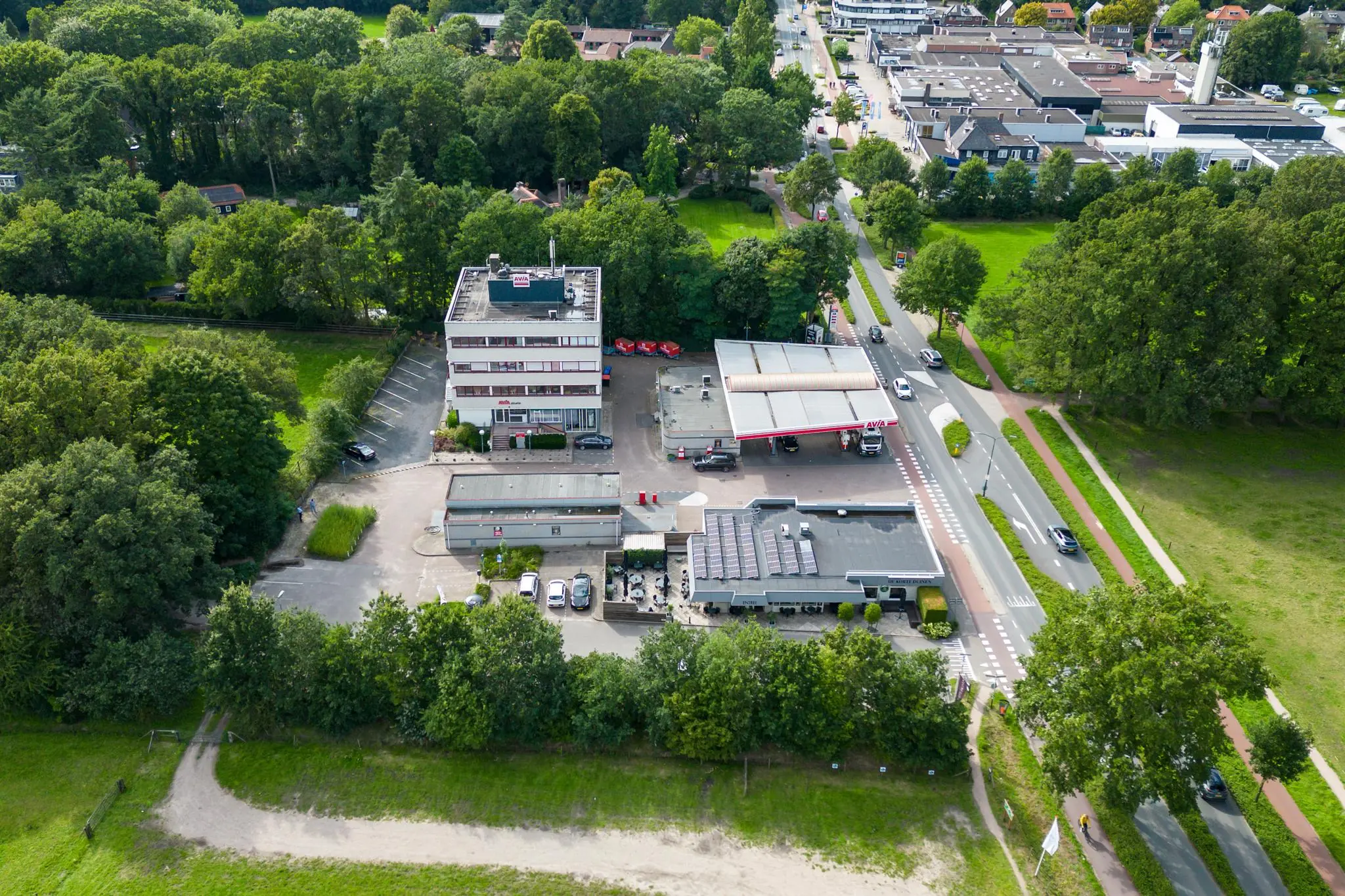 Luchtfoto van een AVIA tankstation met aangrenzend kantoorgebouw en horecagelegenheid aan de Birkstraat, omgeven door groen en nabij een woonwijk.