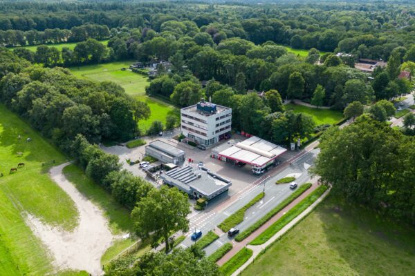 Luchtfoto van een tankstation en kantoorgebouw aan de Birkstraat, omgeven door weilanden en bosrijk gebied.