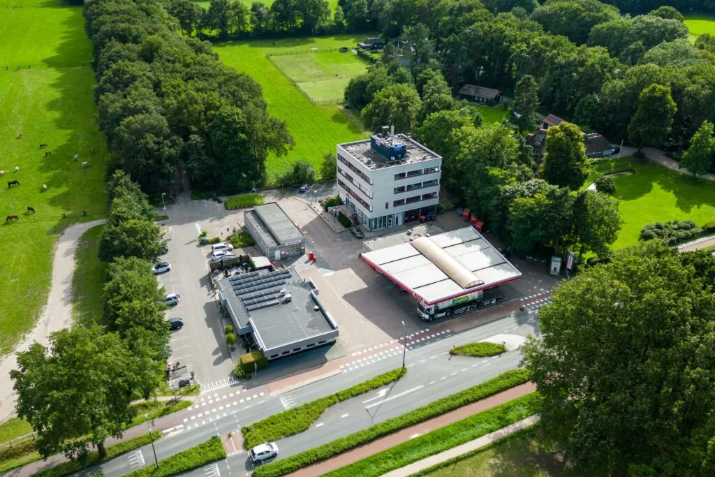 Luchtfoto van een tankstation, kantoorgebouw en omliggend groen aan de Birkstraat.