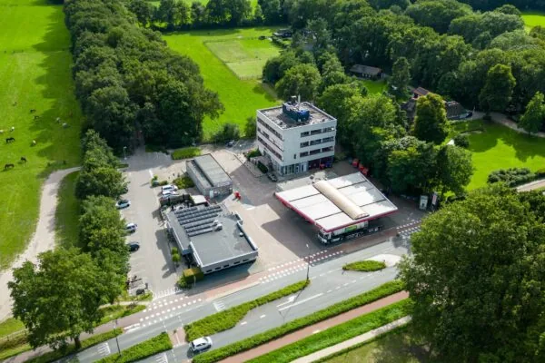 Luchtfoto van een tankstation, kantoorgebouw en omliggend groen aan de Birkstraat.