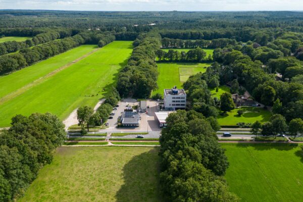 Luchtfoto van de Birkstraat met omliggende weilanden, een bosrijk gebied en een gebouw met parkeerterrein.