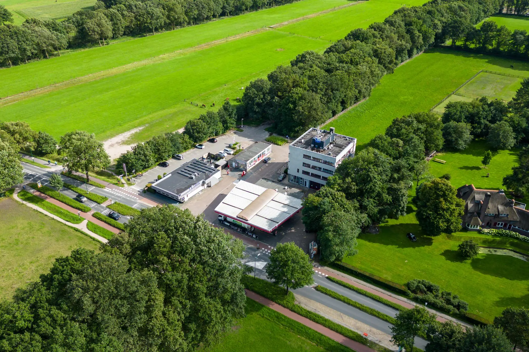 Luchtfoto van gebouwen en een benzinestation aan de Birkstraat, omringd door groene weilanden en bomen.