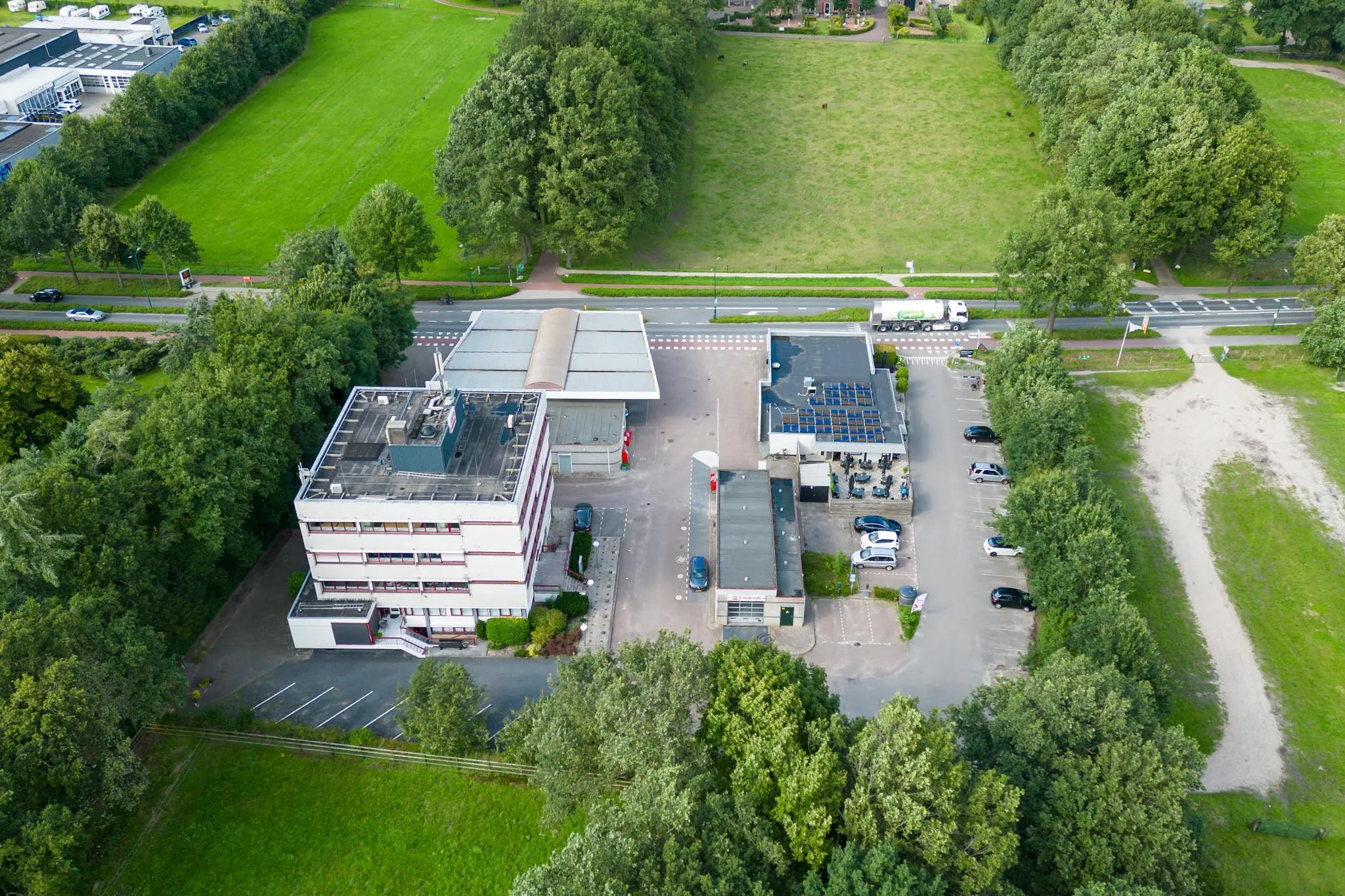 Luchtfoto van een tankstation met bijgebouwen aan de Birkstraat, omgeven door groen en parkeerplaatsen.