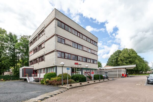 Wit kantoorgebouw aan de Birkstraat met AVIA-station op de voorgrond en parkeerplaats ernaast.