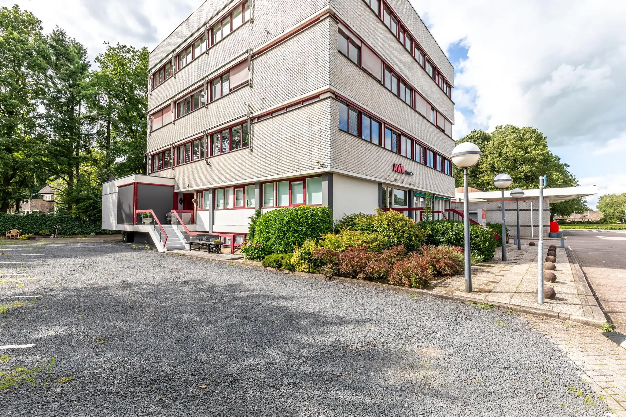 Vooraanzicht van een wit kantoorgebouw aan de Birkstraat met de naam AVIA Studio, omgeven door groen en parkeerplaatsen.