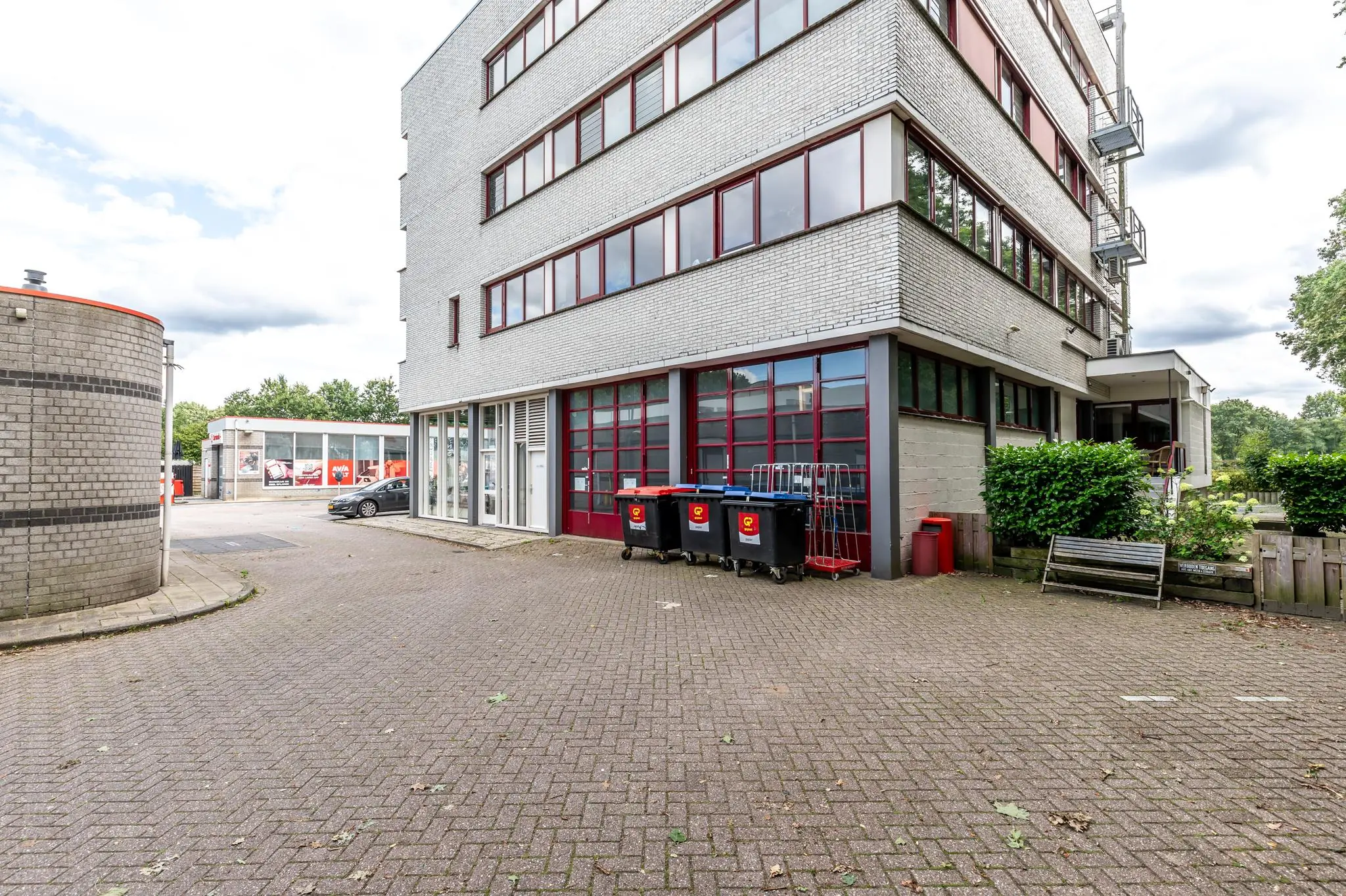 Achterzijde van een kantoorpand aan de Birkstraat met afvalcontainers, een winkel in de verte en een geparkeerde auto.