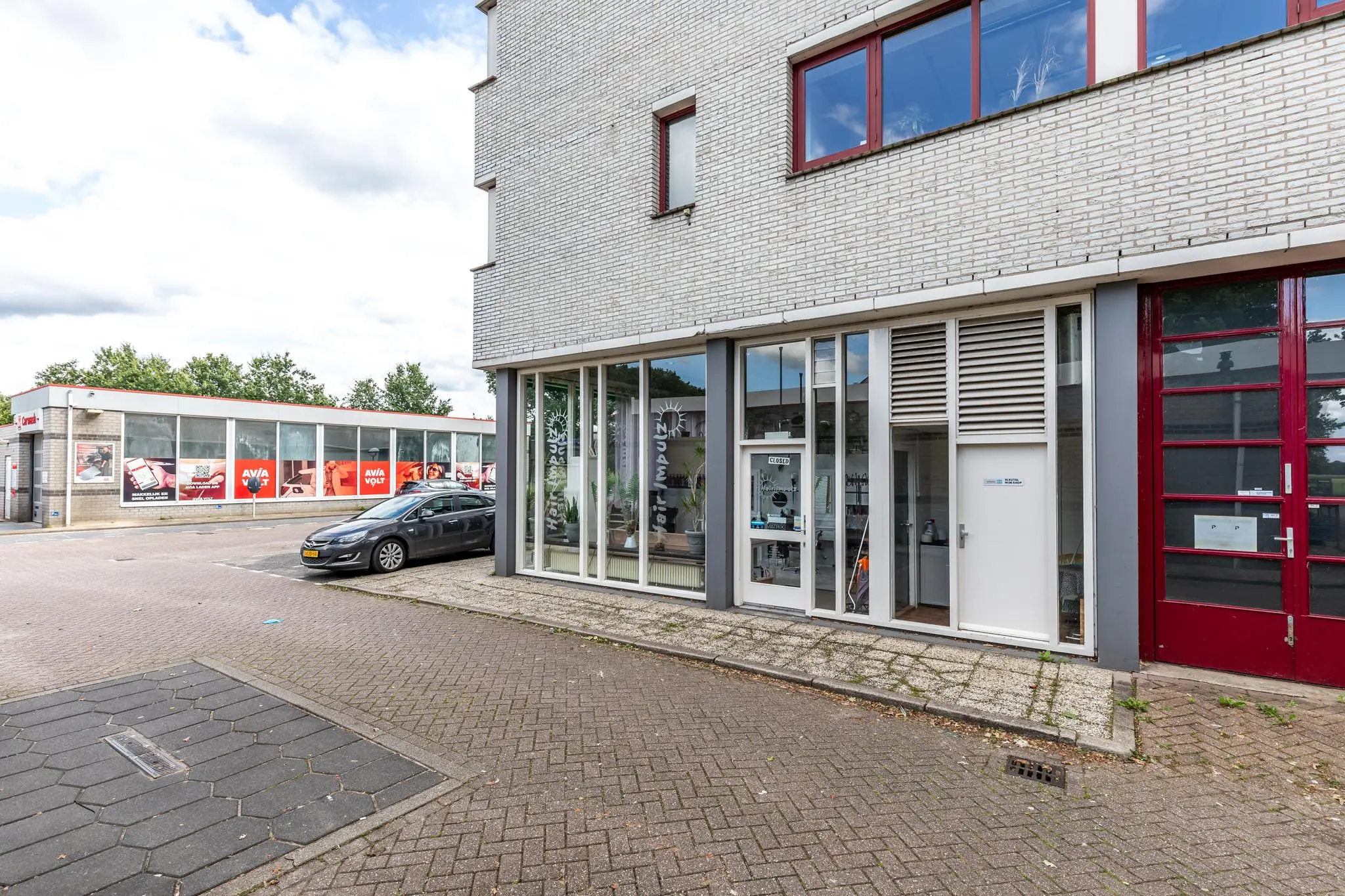 Voorgevel van een bedrijfsruimte aan de Birkstraat met grote ramen, een geparkeerde auto en een AVIA-tankstation op de achtergrond.
