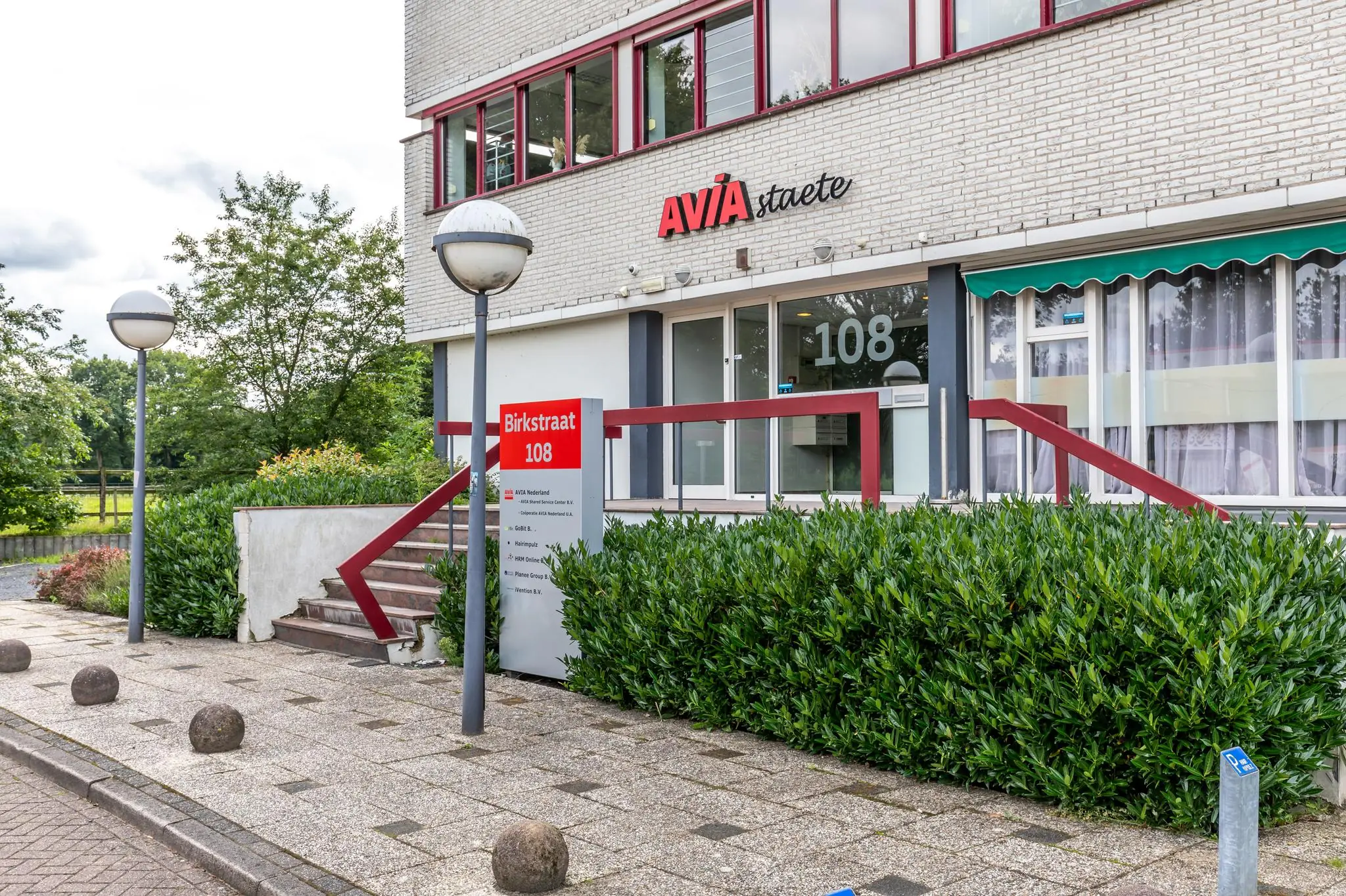 Voorgevel van het kantoorgebouw AVIA Staete aan de Birkstraat 108 met entree, naambord en omliggend groen.
