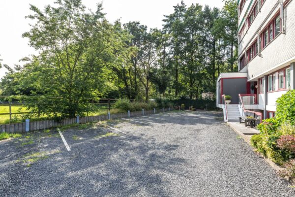 Grindparkeerplaats naast een wit gebouw aan de Birkstraat, omgeven door bomen en groen.