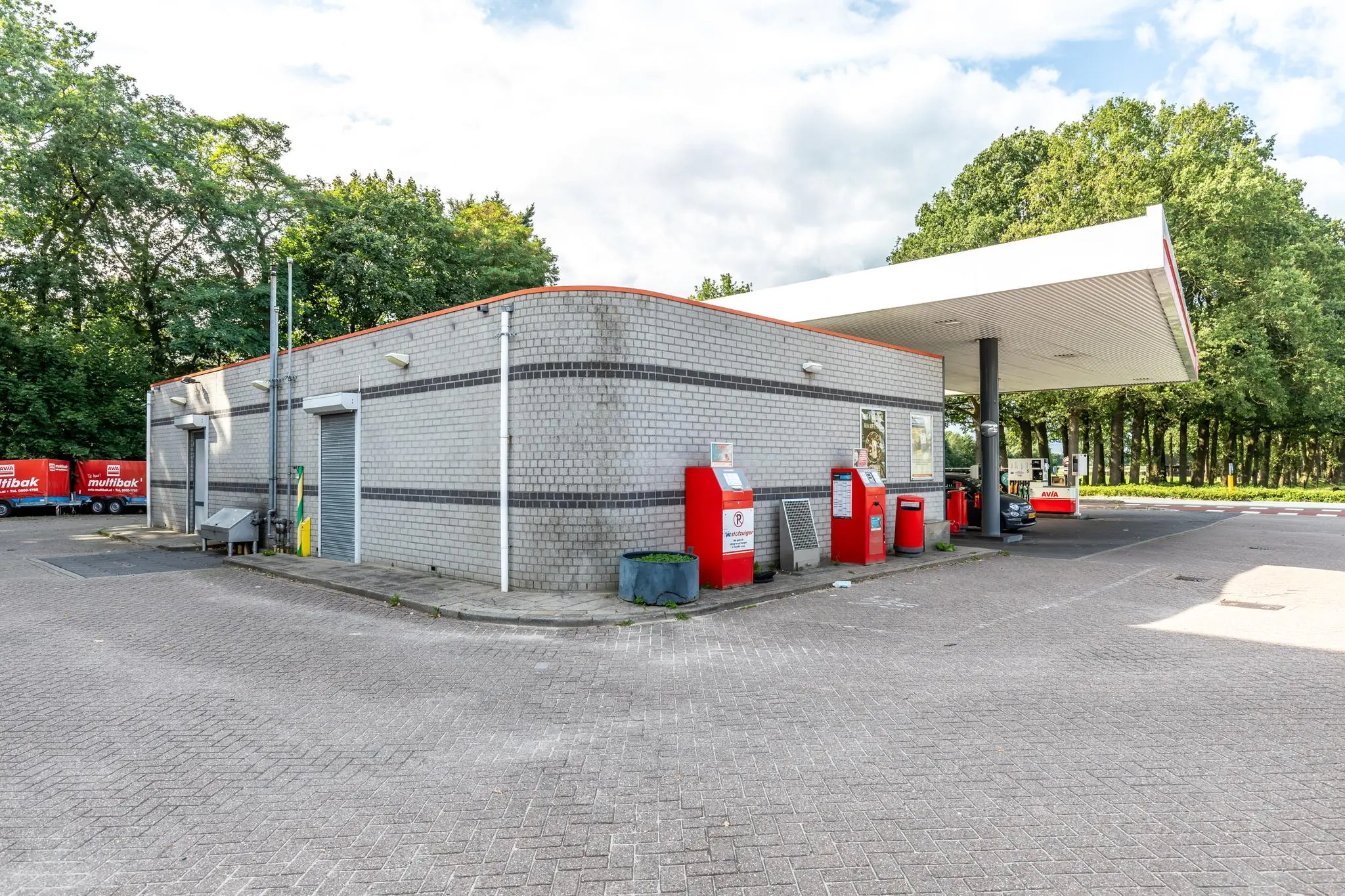 Buitenzicht op een AVIA tankstation aan de Birkstraat met grijs gebouw, rode brievenbus en parkeerapparaat.