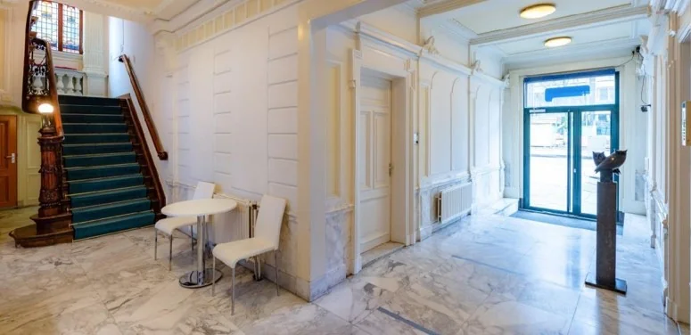 Lichte marmeren entreehal in een klassiek pand aan de Sarphatistraat, met trap, kunstobject en zitgedeelte.