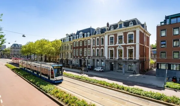 Straatbeeld van de Sarphatistraat in Amsterdam met een passerende tram en statige herenhuizen.