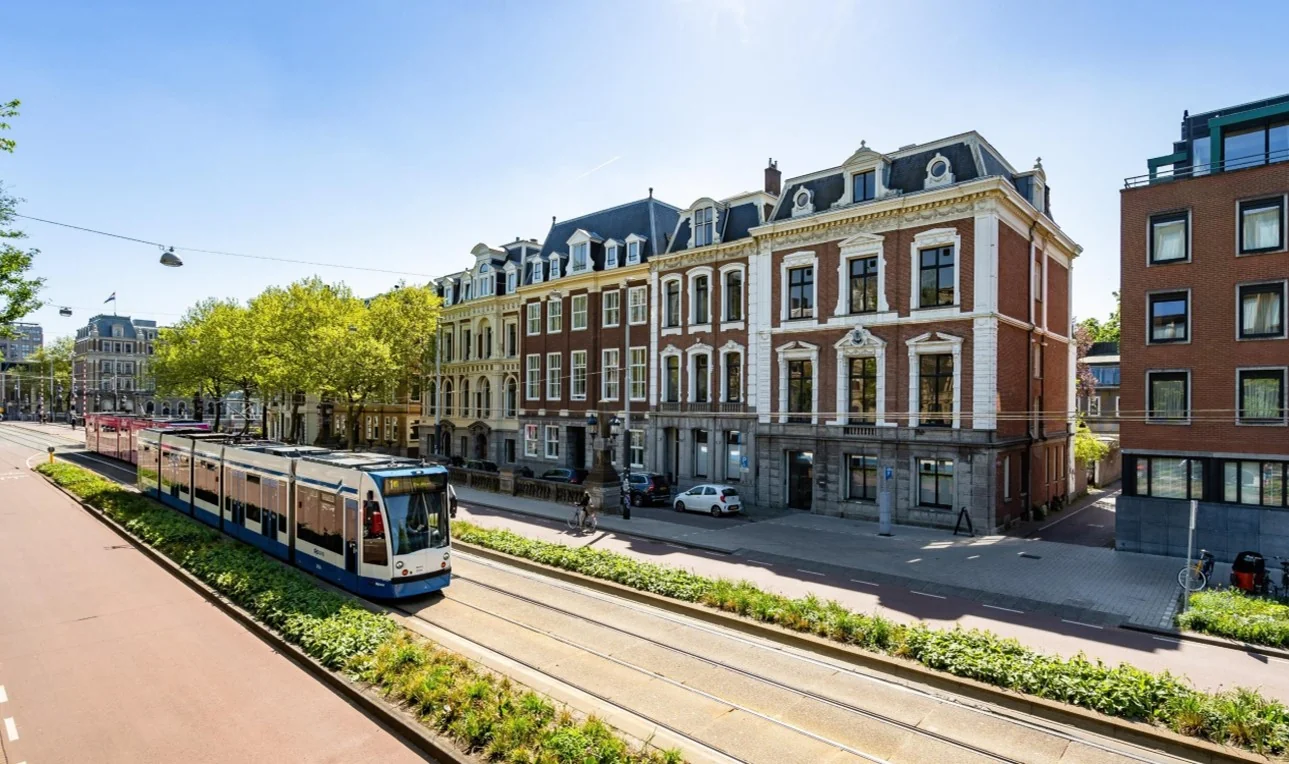 Straatbeeld van de Sarphatistraat in Amsterdam met een passerende tram en statige herenhuizen.