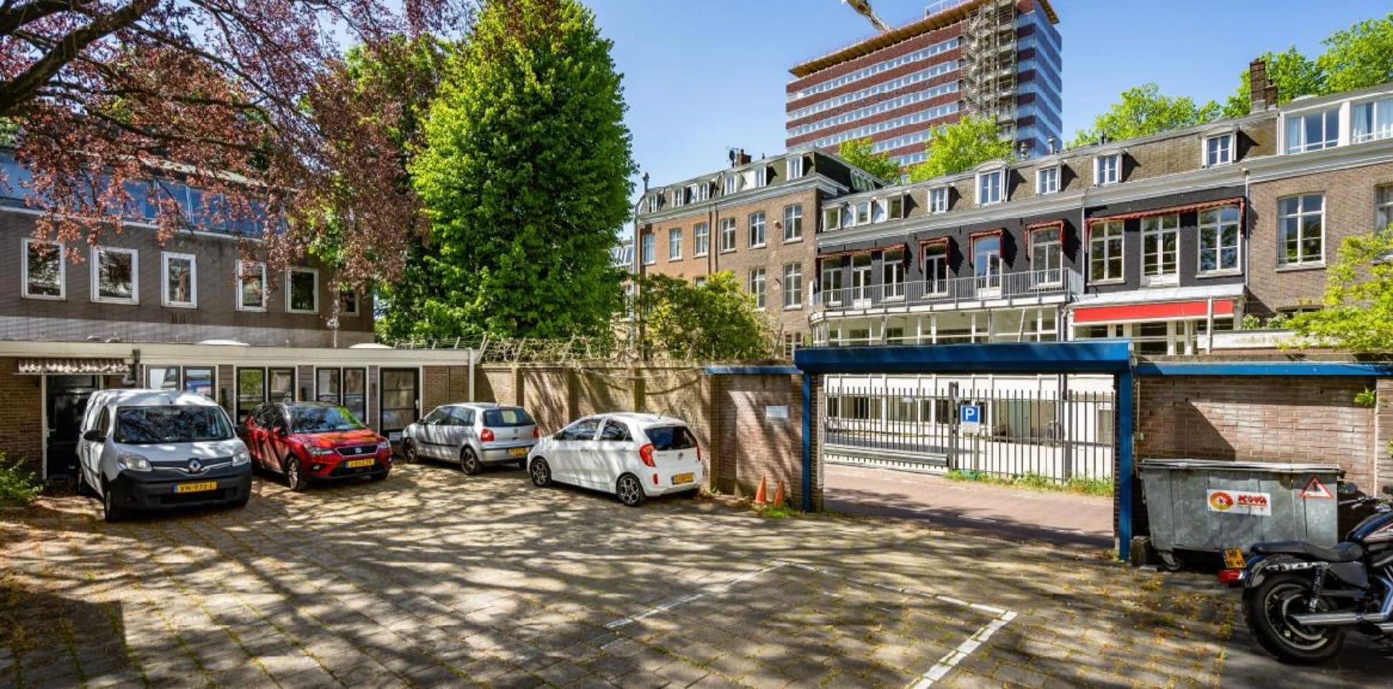 Parkeerplaats aan de Sarphatistraat in Amsterdam met geparkeerde auto's, een gesloten poort en omliggende woongebouwen.