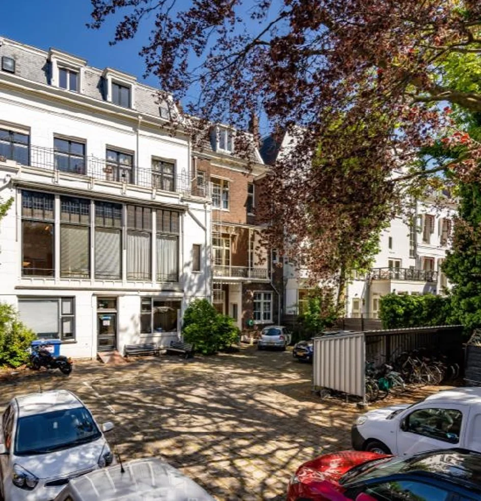 Binnenplaats met geparkeerde auto's en fietsen aan de Sarphatistraat in Amsterdam, omgeven door klassieke herenhuizen.