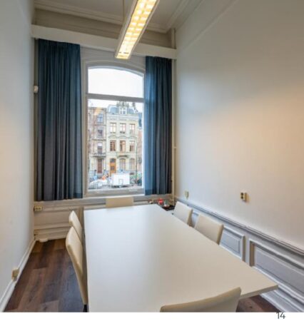 Vergaderruimte met witte tafel en stoelen aan de Sarphatistraat, met uitzicht op klassieke gevels.