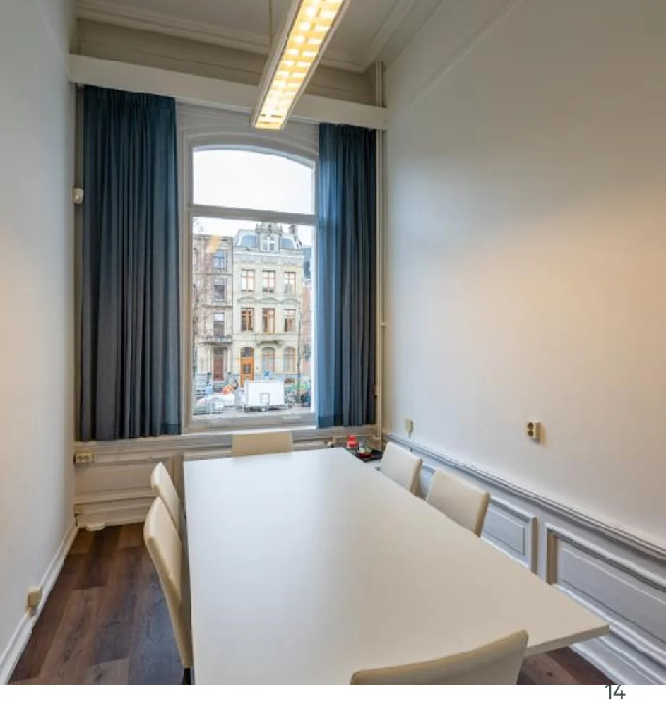 Vergaderruimte met witte tafel en stoelen aan de Sarphatistraat, met uitzicht op klassieke gevels.
