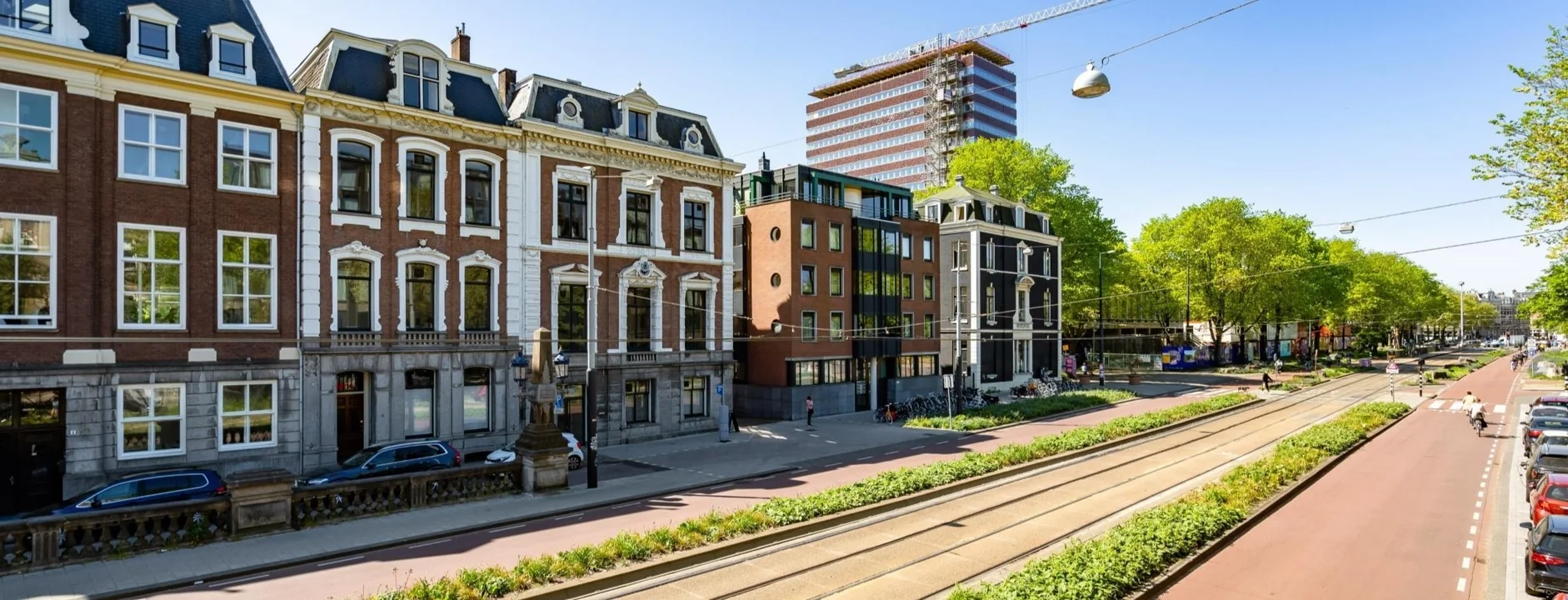 Gevels van historische en moderne panden langs de Sarphatistraat in Amsterdam met trambaan en fietspad op de voorgrond.