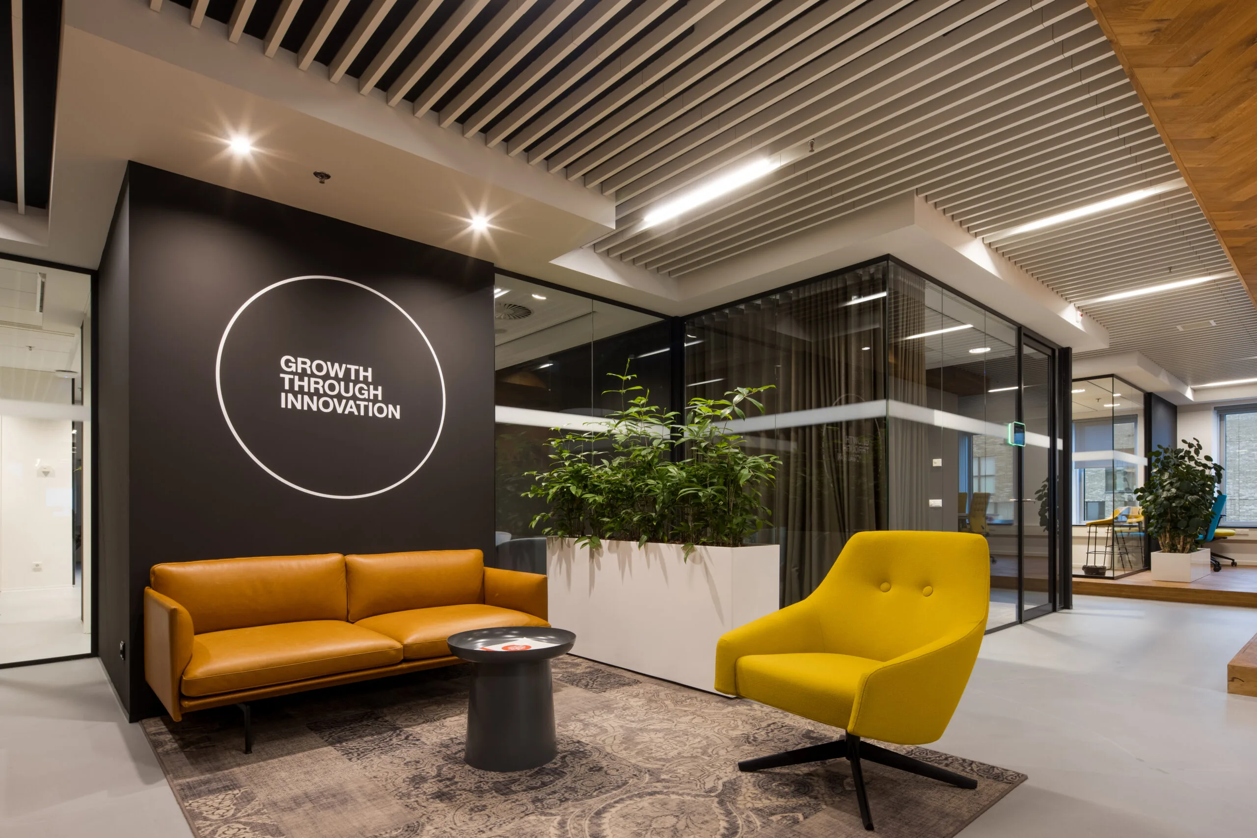 Modern ingerichte kantoorlounge met een gele fauteuil, een bruine leren bank en de tekst "Growth Through Innovation" op een zwarte muur.