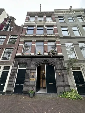 Voorgevel van een klassiek Amsterdams grachtenpand aan de Bloemgracht met moderne ingang en decoratieve poppen op de vensterbank.