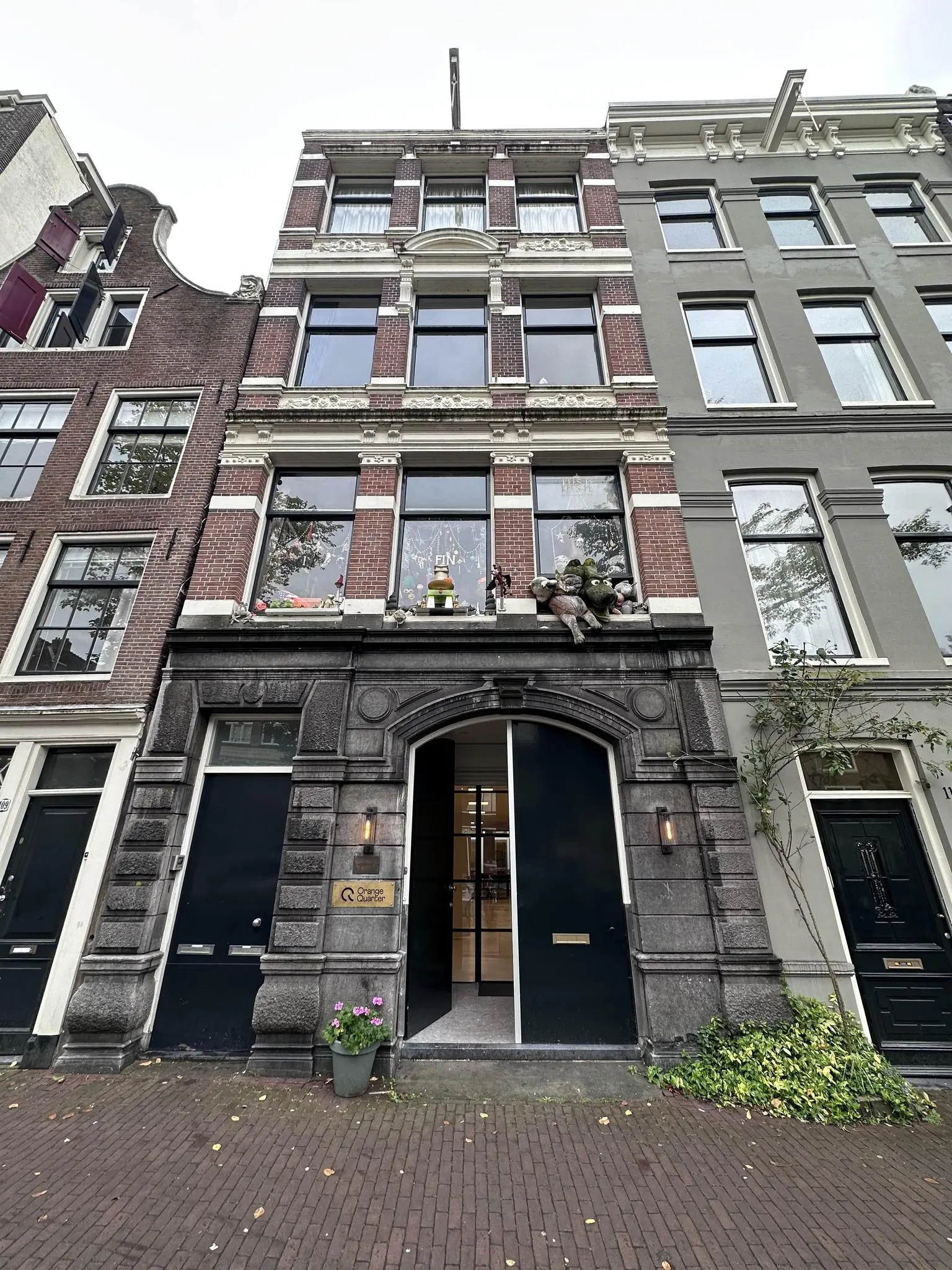 Voorgevel van een klassiek Amsterdams grachtenpand aan de Bloemgracht met moderne ingang en decoratieve poppen op de vensterbank.