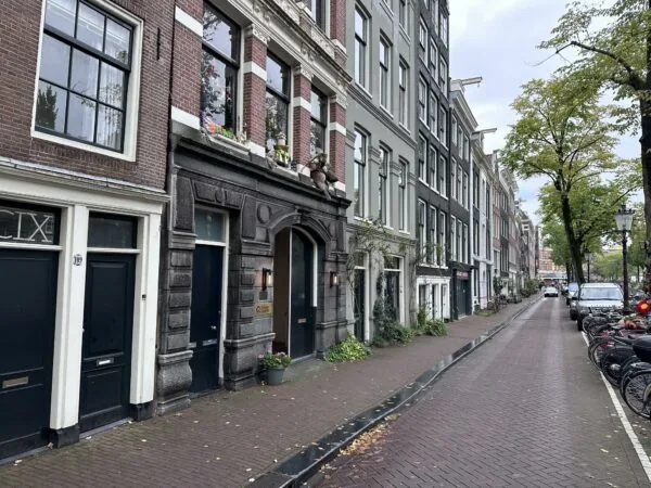 Gevels van karakteristieke grachtenpanden aan de Bloemgracht in Amsterdam met geparkeerde fietsen en auto's langs de straat.