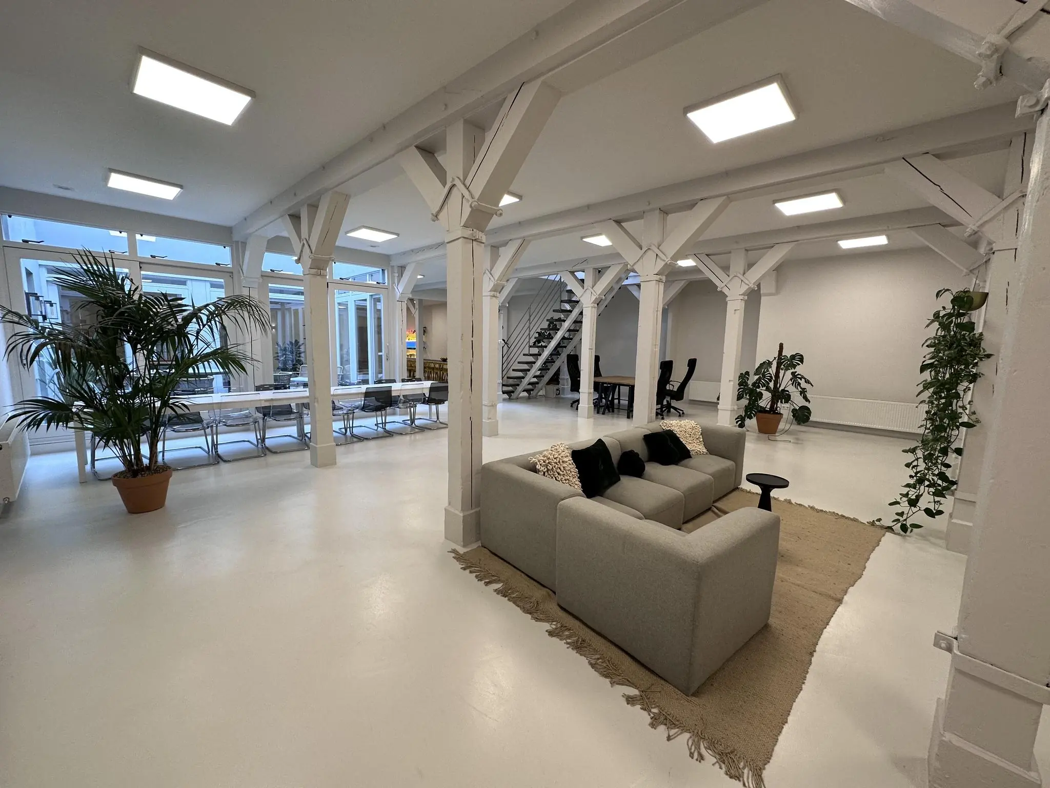 Moderne, open kantoorruimte aan de Bloemgracht met een zithoek, lange vergadertafel, planten en witte balkenconstructie.