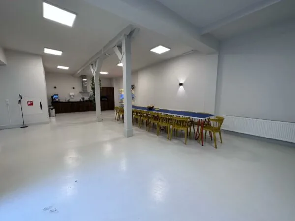 Ruime, modern ingerichte gemeenschappelijke ruimte aan de Bloemgracht met lange tafel, gele stoelen en open keuken.