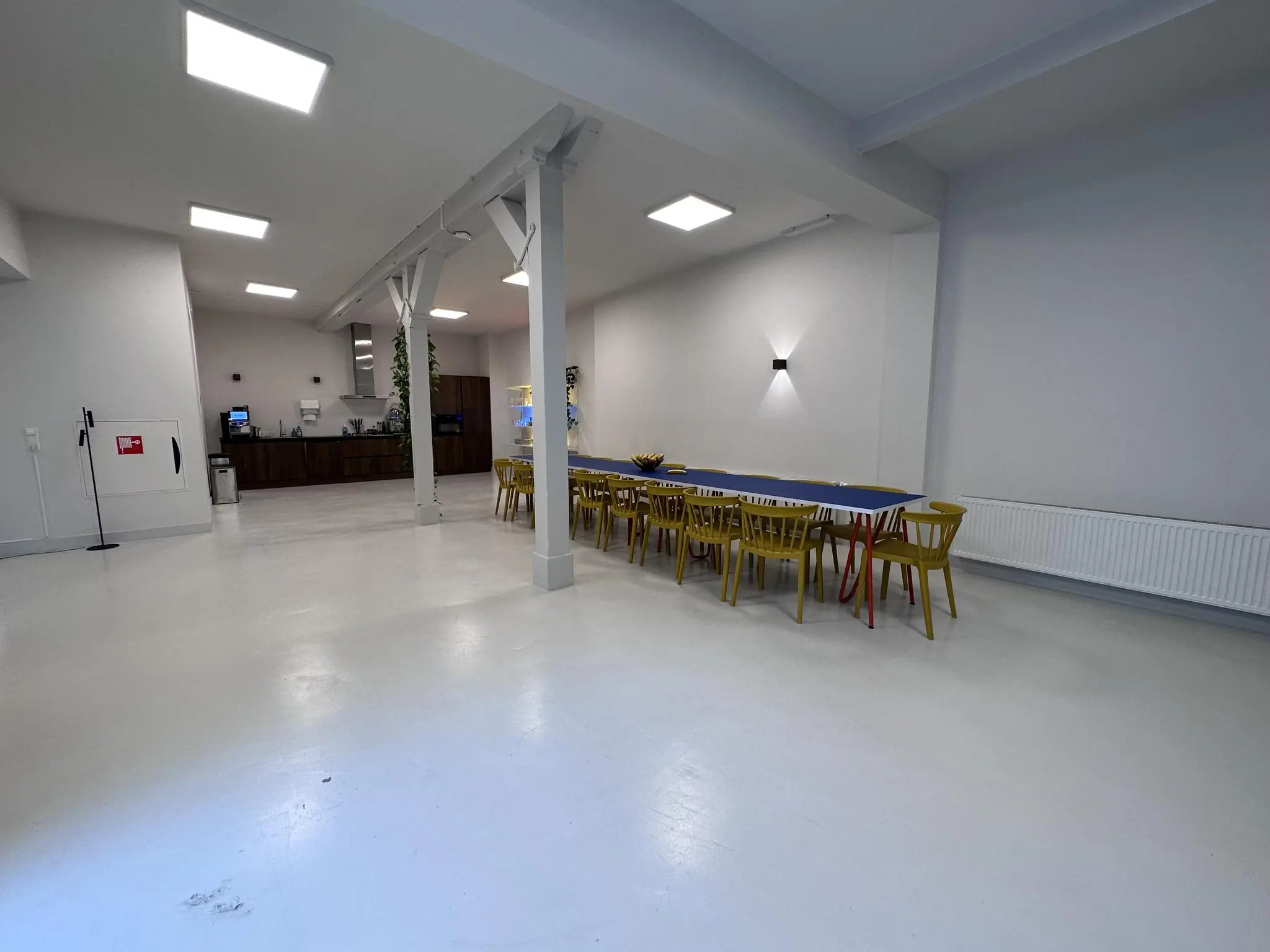 Ruime, modern ingerichte gemeenschappelijke ruimte aan de Bloemgracht met lange tafel, gele stoelen en open keuken.