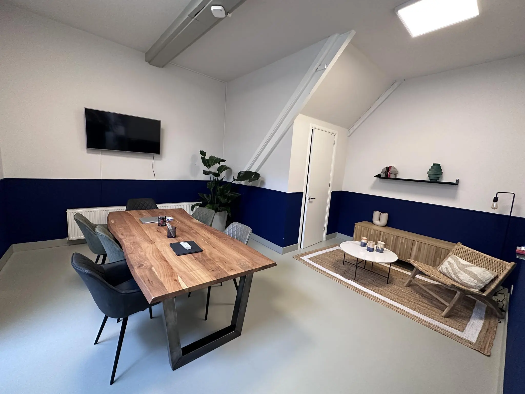 Vergaderruimte aan de Bloemgracht met houten tafel, flatscreen, planten en een knusse zithoek.