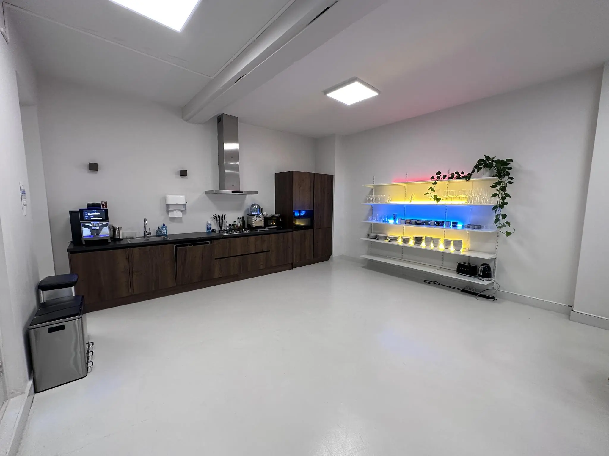 Moderne pantry op Bloemgracht met houten keukenkastjes, een koffiezetapparaat en verlichte wandplanken met servies en glazen.