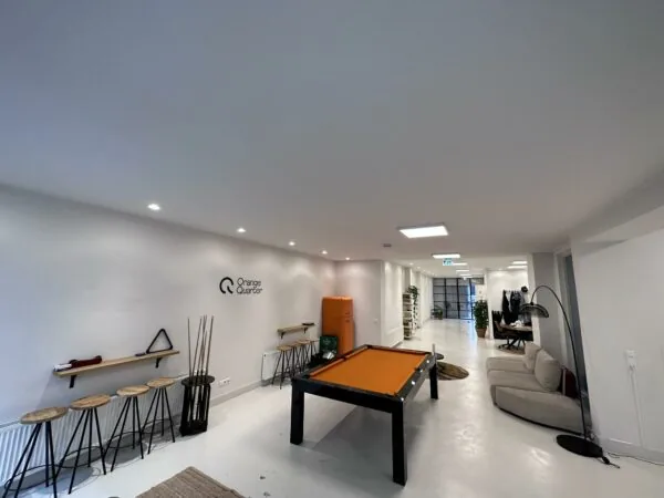 Moderne kantoorruimte van Orange Quarter aan de Bloemgracht met een oranje pooltafel, zitgedeelte en minimalistische inrichting.