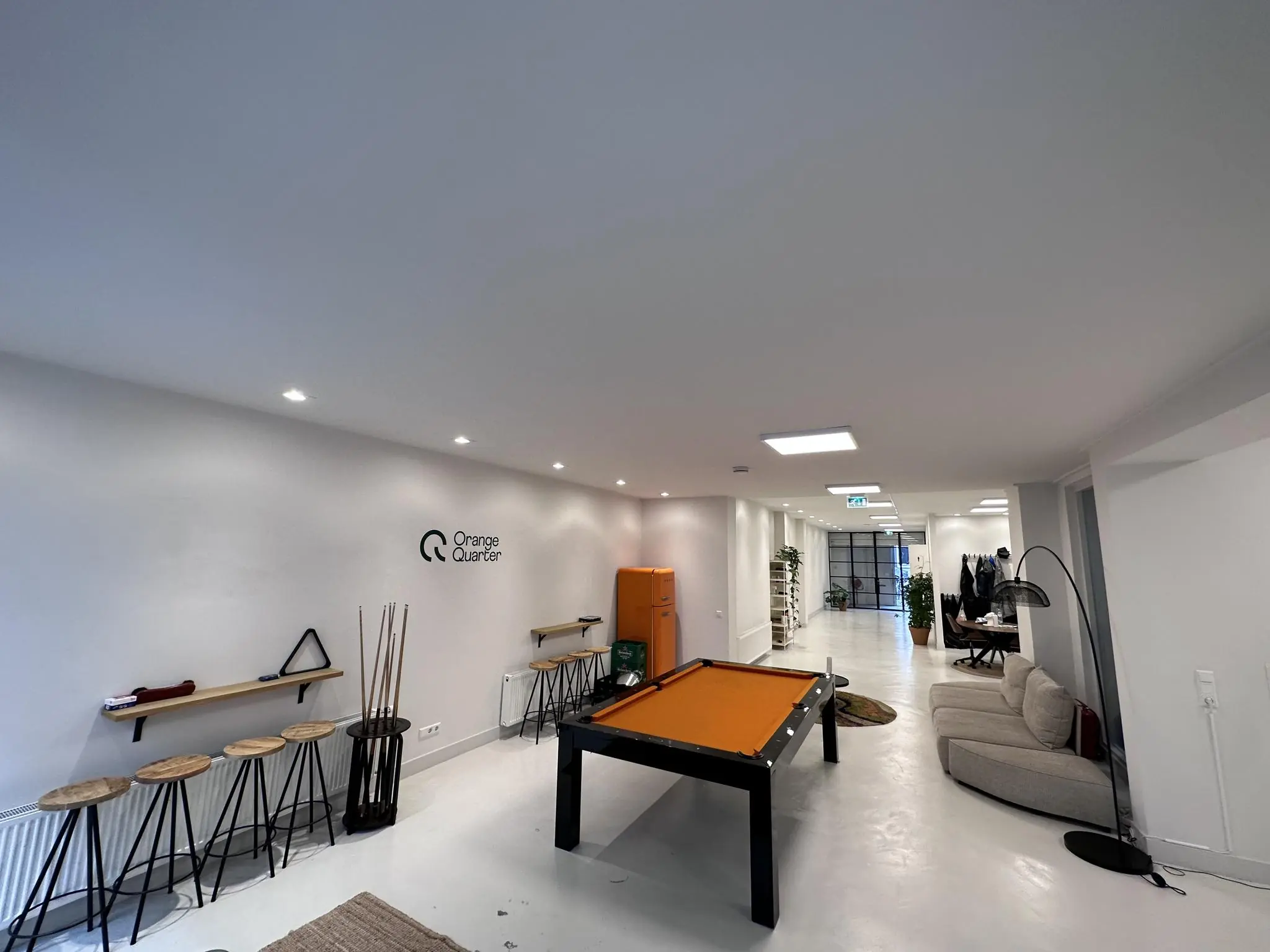 Moderne kantoorruimte van Orange Quarter aan de Bloemgracht met een oranje pooltafel, zitgedeelte en minimalistische inrichting.